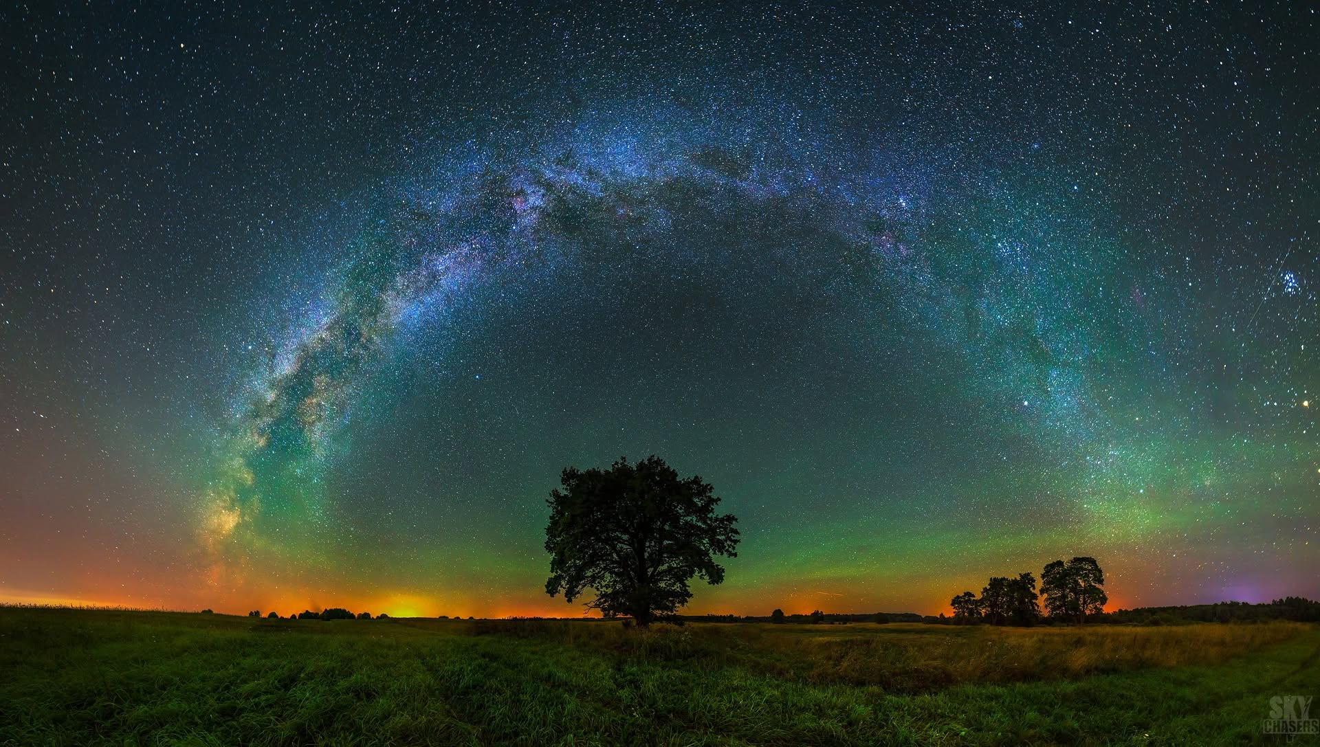 Paukščių tako arka ir žalias atmosferos švytėjimas virš laukų su vienišu medžiu